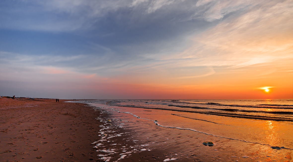 sunset on a stretch of beach with blue and orange sky